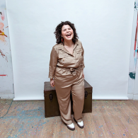 Indigenous artist, Zoey Roys, looking at the camera and laughing while standing in an art studio.